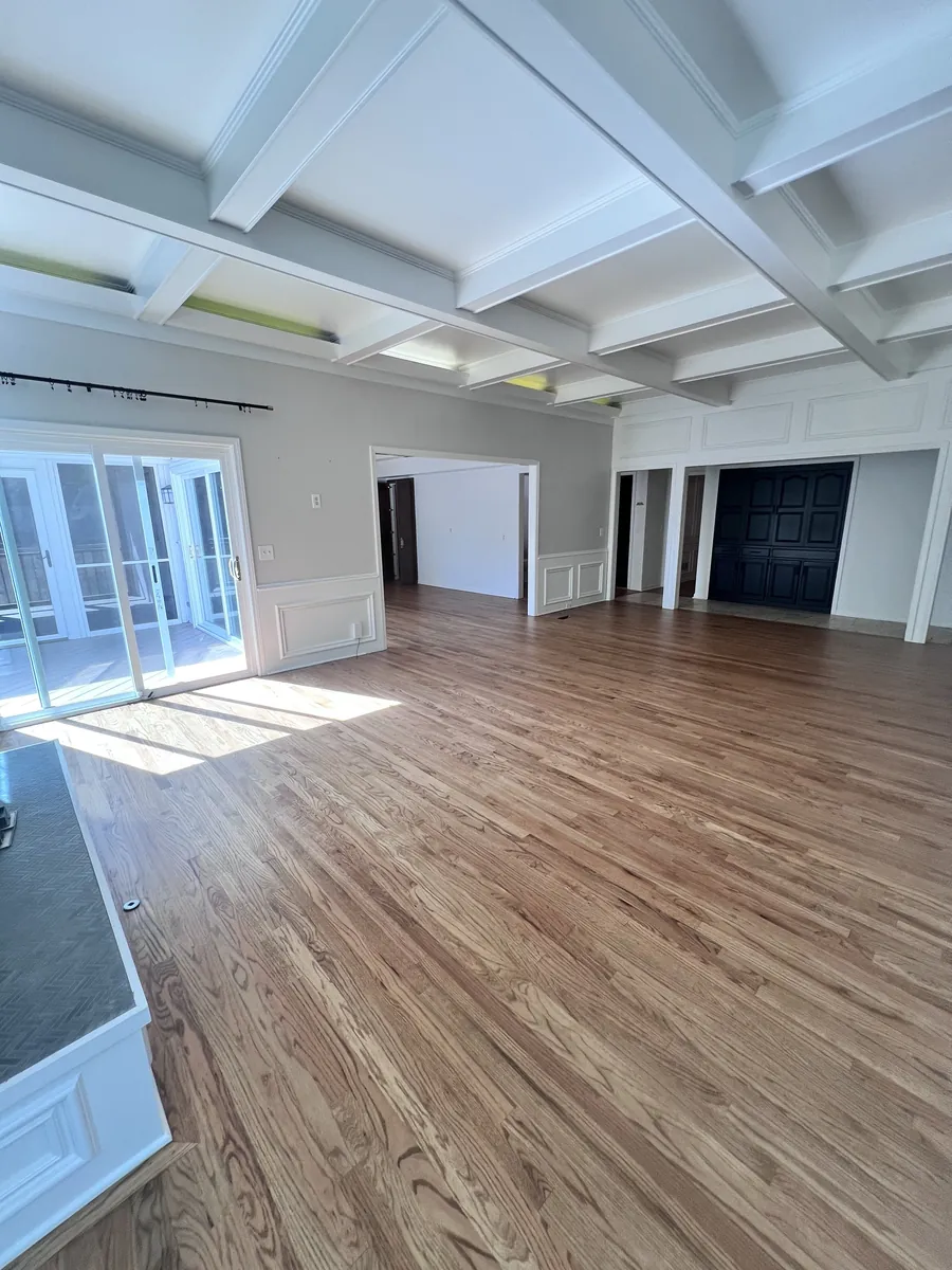 Natural oak hardwood in a sunlit room with a coffered ceiling and white wainscoting